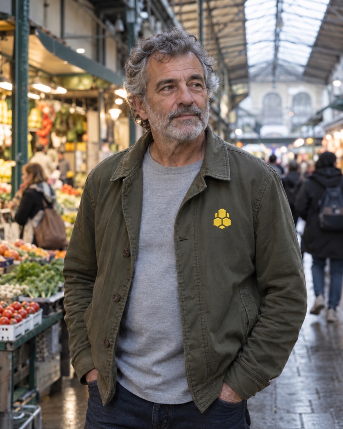 Man in an olive jacket looking thoughtfully across an outdoor market.