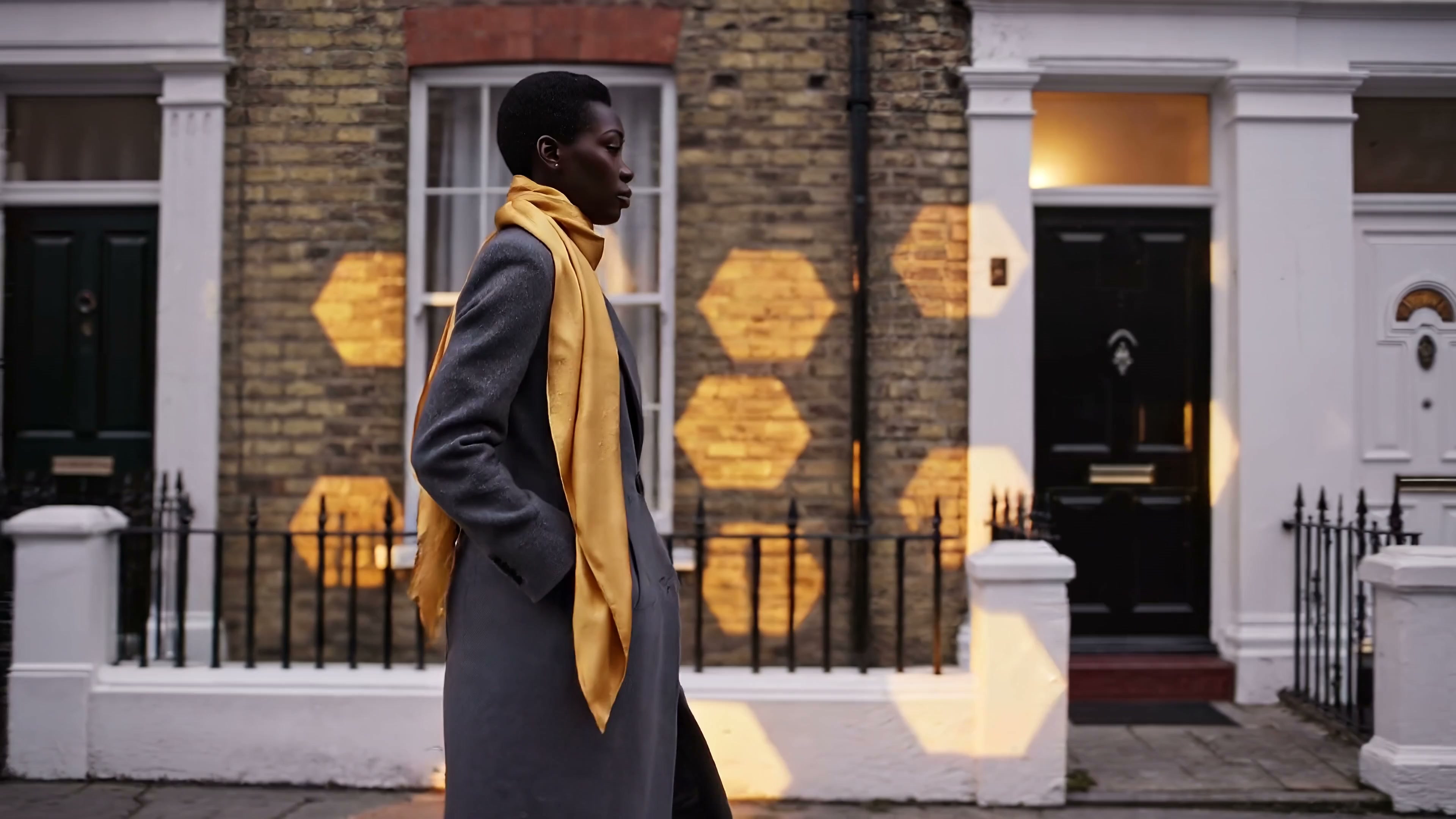 A woman with a yellow scarf walking past warmly lit homes